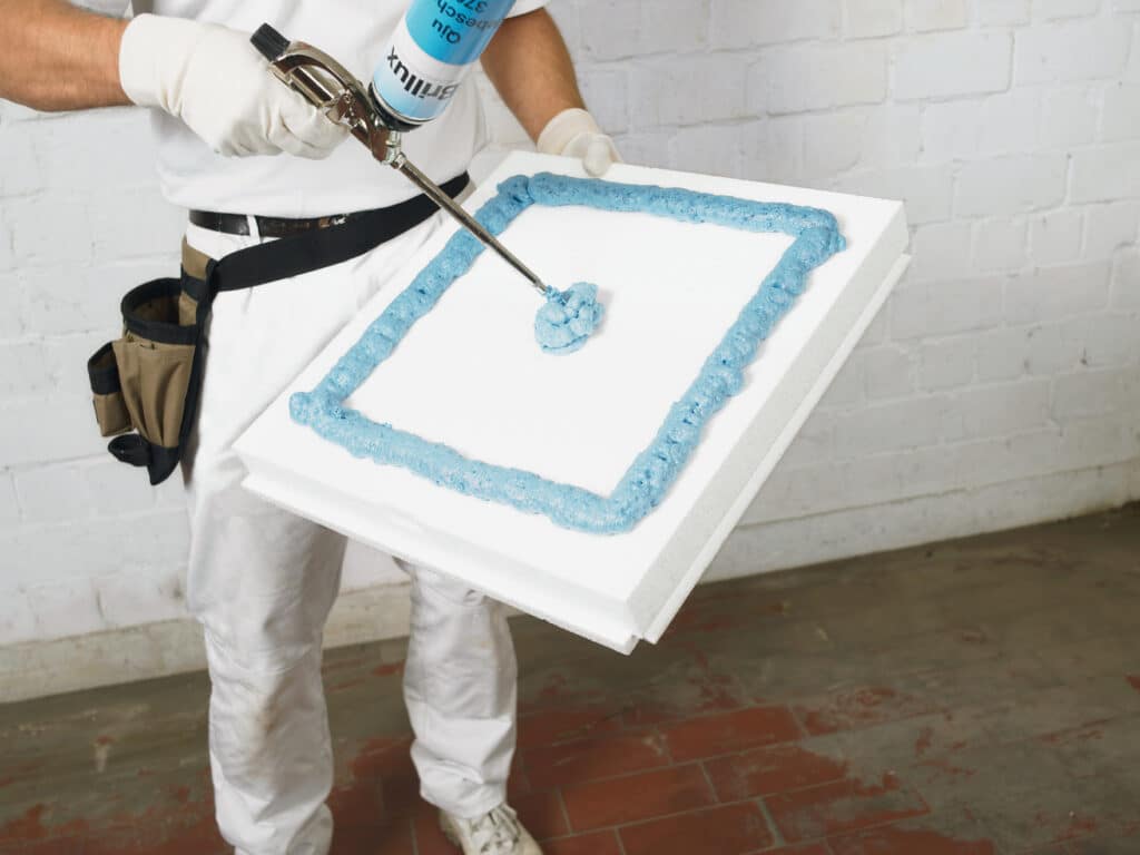 Malerbetrieb CasaColor: Ein Handwerker trägt blauen Schaum auf eine Dämmplatte auf.