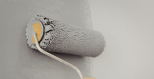 Haus streichen: Eine Fassade wird mit einer Farbrolle grau gestrichen.